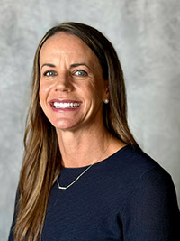 A smiling woman wearing a blue shirt in front of a gray background